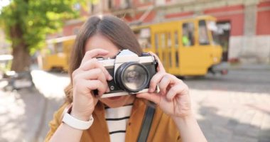 Kasabanın caddesinde kamerayla fotoğraf çeken oldukça mutlu, genç, beyaz bir kız. Açık havada. Neşeli kadın fotoğrafçı güneşli yaz gününde şehir dışında. Arkaplanda tramvay.