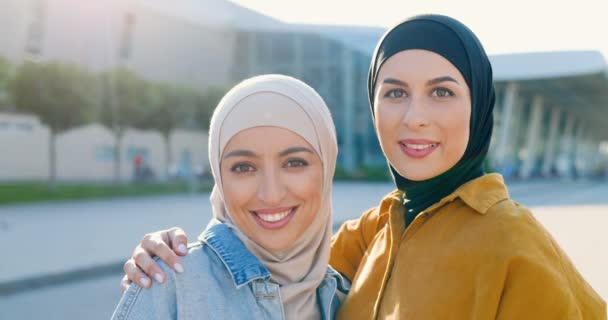 照片上年轻的阿拉伯美女穿着黑色的劫机站在街头 对着镜头微笑 穿着传统阿拉伯头巾的漂亮的穆斯林女性紧紧地拥抱在一起 — 图库视频影像