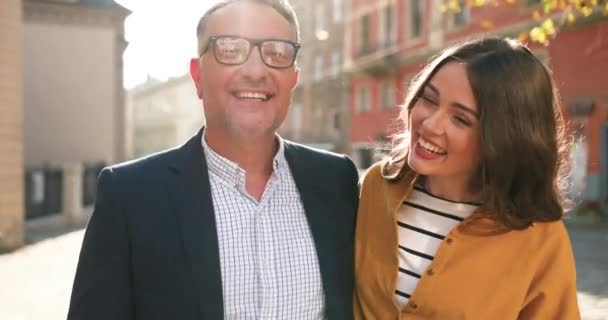 Ritratto di felice padre caucasico con gli occhiali che cammina per strada e ride con una figlia adulta piuttosto giovane. All'aperto. Uomo e ragazza con sorrisi gioiosi passeggiando nella giornata di sole. La paternità — Video Stock