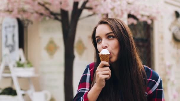 Retrato de una hermosa mujer europea comiendo helado en taza de gofres de pie en la calle. Linda chica morena come postre y disfruta del buen tiempo. — Vídeos de Stock