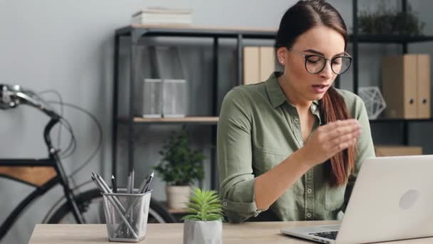 Joven hermosa mujer con gafas de trabajo en el ordenador portátil. Trabajadora bosteza mientras está sentada en su escritorio en la oficina moderna. — Vídeos de Stock