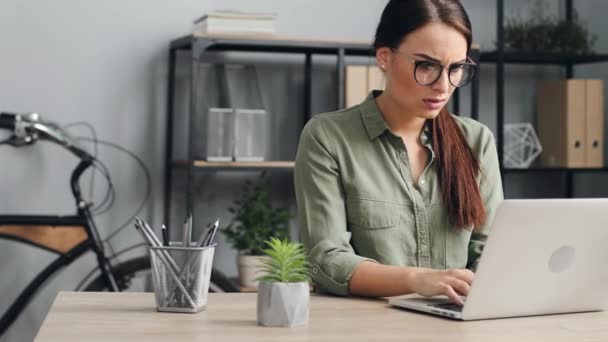 Junge schöne Frau mit Brille, die am Laptop arbeitet. Arbeiterin arbeitet hart am Computer im modernen Büro im Loft-Stil. — Stockvideo