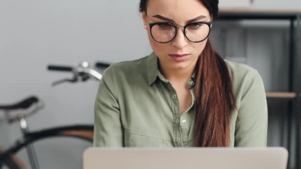 Primer plano de la joven hermosa mujer con gafas de trabajo en el ordenador portátil. La trabajadora mira fijamente a la pantalla del portátil. — Vídeo de stock