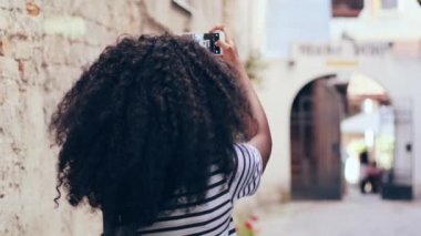 Kıvırcık saçlı Afrikalı Amerikalı turist kıza yakın durun. Gözlüklü güzel bir kadın. Yeni şehrin mimari simgelerinin fotoğrafını çekiyor. Arkadan görüntüle.