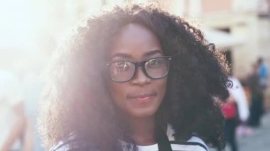 Güneş ışığında şehir merkezinde dikilen güzel Afrikalı Amerikalı kadın portresi. Kar beyazı gülüşü ve kameraya poz vererek gülümseyen genç bayan turist..