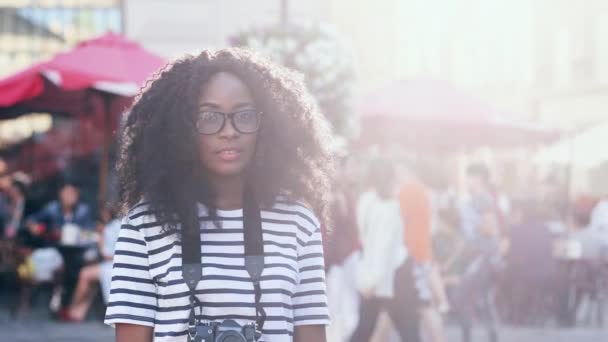 Közelkép a gyönyörű afro-amerikai nő göndör haj áll a város központjában napfényben.Fiatal női turista mosolyog és pózol a kamera. — Stock videók