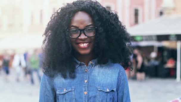 Retrato de jovem estudante de intercâmbio feliz com cabelo encaracolado exuberante. Menina bonita em camisa jeans fala à câmera e acena a bandeira da Grã-Bretanha na rua. — Vídeo de Stock