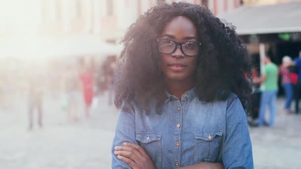 Retrato de mujer joven sonriente en gafas con pelo rizado exuberante. Hermosa chica en camisa de mezclilla cruzó sus brazos sobre su pecho y mirando a la cámara. — Vídeos de Stock