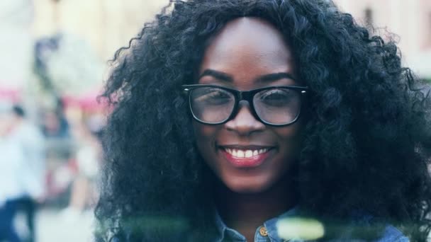 Siyah kıvırcık saçlı, gözlüklü Afro-Amerikan bir kadının portresini yakından çek. Güzel kız kameraya bakıyor ve beyaz dişlerle gülümsüyor.. — Stok video