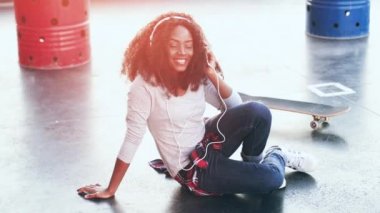 Beyaz kulaklıklarla terasta oturan neşeli Afro-Amerikalı kız müzik dinliyor. Genç hippi kız elinde telefonla melodinin ritmine göre hareket ediyor..