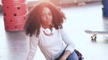 Terasta oturmuş gülümseyen kameraya bakan neşeli Afrikalı Amerikalı kız portresi. Gün batımında çatıda poz veren gür siyah kıvırcık saçlı güzel kız..