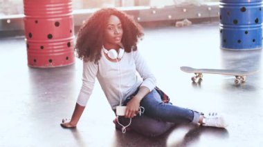 Terasta oturmuş gülümseyen kameraya bakan Afro-Amerikan kadının portresi. Gün batımında çatıda poz veren gür siyah kıvırcık saçlı şık bir kız. Genel plan.