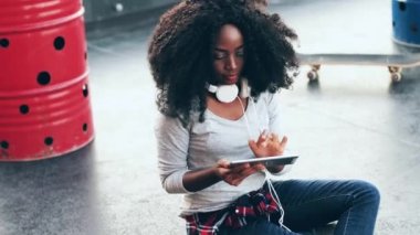 Kıvırcık saçlı neşeli genç kadın terasta oturuyor ve dışarıda tabletle internetten alışveriş yapıyor. Çatıda oturan güzel Afrikalı Amerikalı kadın elektronik cihaz kullanmaktan zevk alıyor..