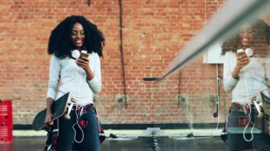 Terasta duran ve mutlu bir ifadeyle akıllı telefona mesaj yazan güzel bir kız. Duvarın yanında kaykayı olan Afrikalı Amerikalı bir kadının portresi..