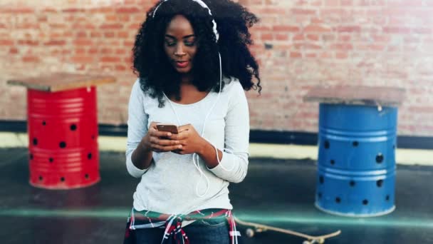 Egy fiatal afro-amerikai nő portréja, aki a teraszon áll és üzenetet ír az okostelefonjára. A csinos lány felnéz a kamerába és mosolyog.. — Stock videók