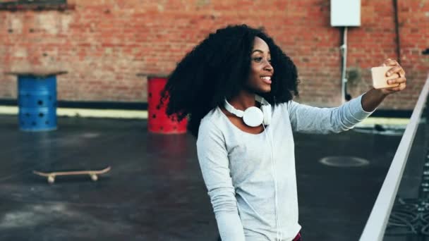 Wesoła młoda kobieta z kręconymi włosami na tarasie nagrywająca wideo na swoim smartfonie. Piękna Afroamerykanka stojąca na dachu rozmawiająca przez telefon wideo. — Wideo stockowe