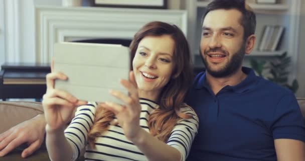 Счастливая семейная пара записывает видео сообщения на планшет. Два человека записывают видео приветствия на устройство, сидя на диване. — стоковое видео