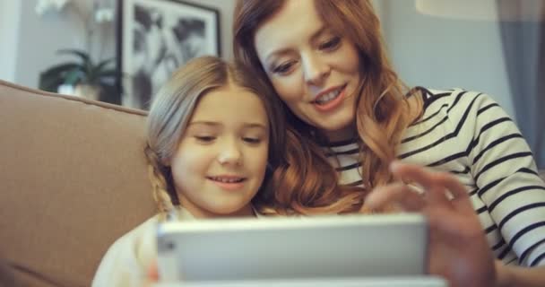 Mladá matka vesele něco vysvětlovala své dceři pomocí digitálního tabletu. Domácí výuka s elektronickým zařízením.