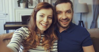 POV mutlu çifti evde video mesajı kaydediyor. İki kişi webcam 'e bakıyor ve gülümsüyor. Neşeli eş tutma cihazı. Kameradan görüntüle.