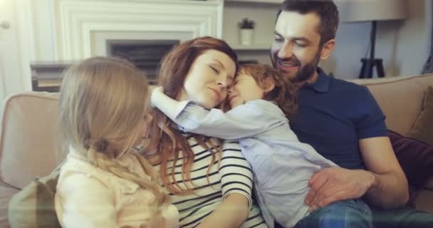 Glada föräldrar med söta förskolebarn kopplar av på soffan. Mamma pappa son och dotter umgås och kramas. — Stockvideo