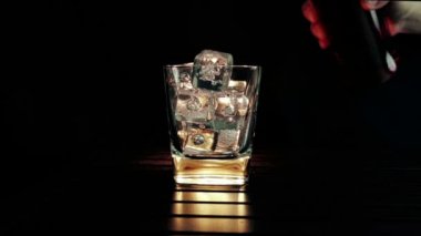 barmen ahşap masa ve siyah koyu arka plan üzerinde buz küpleri ile cam içine dökme viski, buz küpleri, viski odak dinlenmek zaman sıcak bir atmosfer