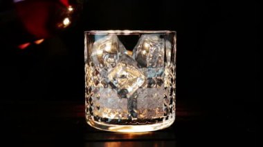 barmen ahşap masa ve siyah koyu arka plan üzerinde buz küpleri ile cam içine dökme viski, buz küpleri, viski odak dinlenmek zaman sıcak bir atmosfer