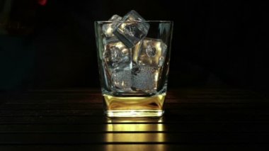 barmen ahşap masa ve siyah koyu arka plan üzerinde buz küpleri ile cam içine dökme viski, buz küpleri, viski odak dinlenmek zaman sıcak bir atmosfer