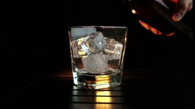barmen ahşap masa ve siyah koyu arka plan üzerinde buz küpleri ile cam içine dökme viski, buz küpleri, viski odak dinlenmek zaman sıcak bir atmosfer