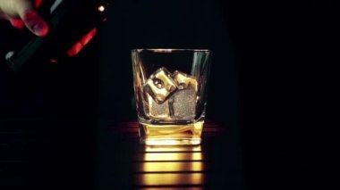 barmen ahşap masa ve siyah koyu arka plan üzerinde buz küpleri ile cam içine dökme viski, buz küpleri, viski odak dinlenmek zaman sıcak bir atmosfer