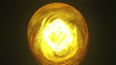 Dönüşün üst kısmı yavaş çekimde tozla açılıp kapanıyor, eski teknolojiye sahip eski tip bir ampul. Ilık sarı renkli ve siyah arkaplanlı, eski model.