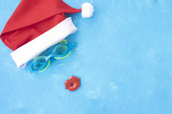 Sombrero de Santa Claus con gafas para nadar y labios rojos. Vacaciones de Navidad, sandalias y gafas de baño junto al agua, zapatillas y gafas de piscina cerca de la piscina — Foto de Stock