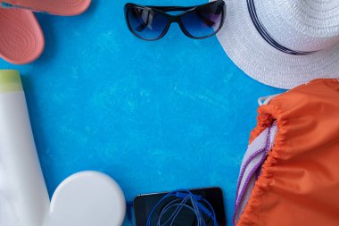 Yaz tatili konsepti, yaz seyahati aksesuarları açık mavi arka planda uzanan şapka, güneş kremi ve metin için fotokopi alanı olan telefon.