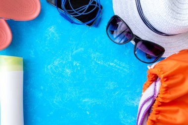 Yaz tatili konsepti, yaz seyahati aksesuarları açık mavi arka planda uzanan şapka, güneş kremi ve metin için fotokopi alanı olan telefon.