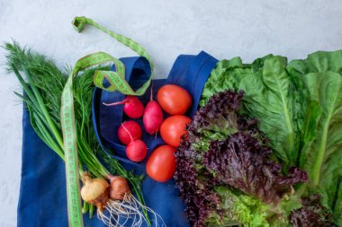 Gri arka planda taze sebzeler. Aromatik otlar, taze fitness sebzeleri salatalıklar ve domatesler, turplar ve soğanlar, salata..