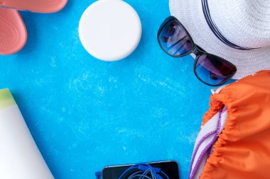 Yaz tatili konsepti, yaz seyahati aksesuarları açık mavi arka planda uzanan şapka, güneş kremi ve metin için fotokopi alanı olan telefon.