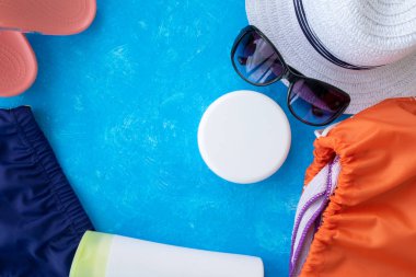 Yaz tatili konsepti, yaz seyahati aksesuarları açık mavi arka planda uzanan şapka, güneş kremi ve metin için fotokopi alanı olan telefon.