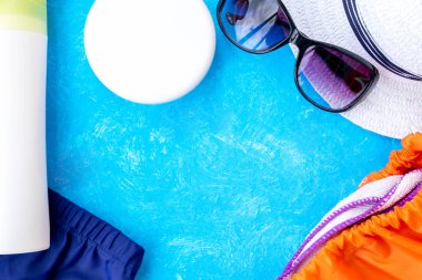 Yaz tatili konsepti, yaz seyahati aksesuarları açık mavi arka planda uzanan şapka, güneş kremi ve metin için fotokopi alanı olan telefon.