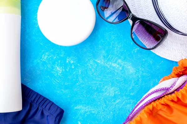 Yaz tatili konsepti, yaz seyahati aksesuarları açık mavi arka planda uzanan şapka, güneş kremi ve metin için fotokopi alanı olan telefon.