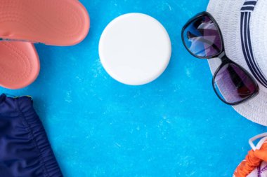 Yaz tatili konsepti, yaz seyahati aksesuarları açık mavi arka planda uzanan şapka, güneş kremi ve metin için fotokopi alanı olan telefon.