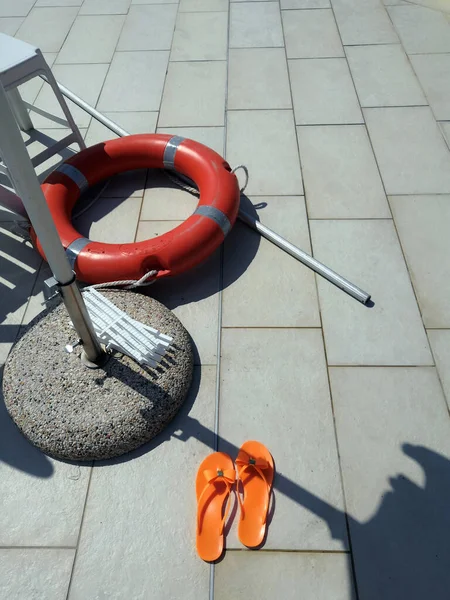 Életmentő felszerelés, narancssárga mentőöv kötéllel a falon lóg a medence mellett. — Stock Fotó