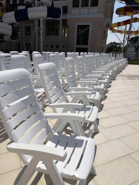 white plastic deck chairs standing in front of each other near the swimming pool with blue tile