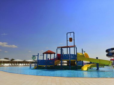 BURGAS AQUA Park, BULGARY - 07.2019. Çocuklar, temiz suyla havuza inen farklı renklerde bir parkta kayıyorlar. Su parkı boş, çocuklar inişe geçiyor.