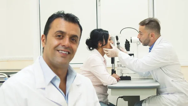 Un médecin souriant s'assoit tandis que sur le fond un autre médecin examine le patient — Photo