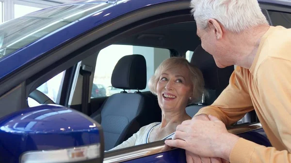 Senior couple poses with car at the dealership