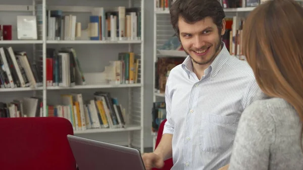 Estudiante masculino muestra a su compañera de clase algo en el portátil de la biblioteca — Foto de Stock