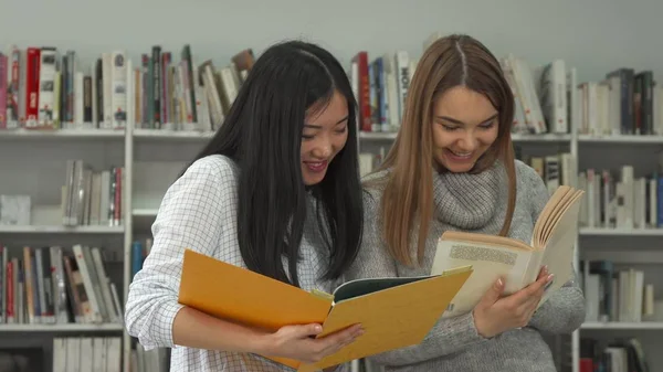 Dos alumnas comparan información en dos libros de la biblioteca —  Fotos de Stock