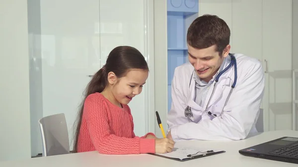 Niña dibuja en portapapeles cerca del médico — Foto de Stock