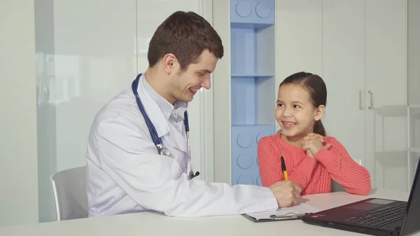 Pediatrician draws on clipboard near the little girl — Stock Photo, Image