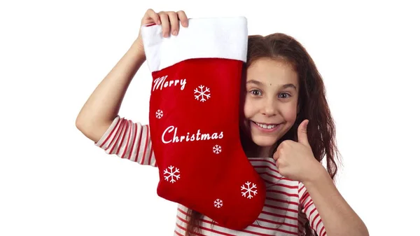 La petite fille jette un coup d'oeil par derrière chaussette avec des cadeaux et montre pouces vers le haut — Photo