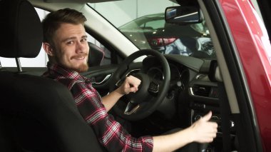 Neşeli yakışıklı erkek müşteri yeni bir araba galerisinde oturan yukarı başparmak gösterilen